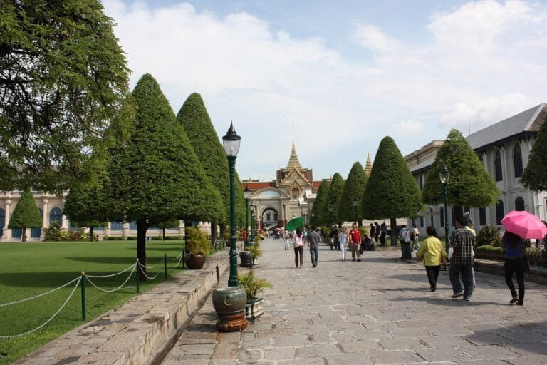 Visitors on a path between clipped trees in palace grounds in Bangkok, Thailand