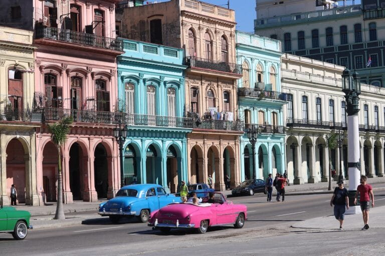 Classic American cars on a Havana street lined with pastel buildings, Cuba