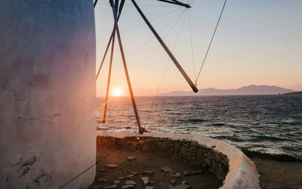 The sun setting beside a traditional windmill in Mykonos, Greece