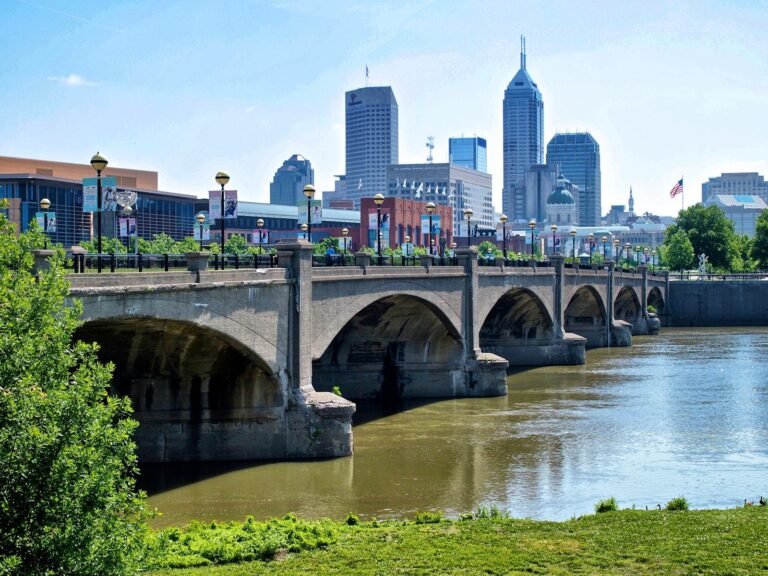A stone arch bridge over the White River with the Indianapolis skyline rising behind it