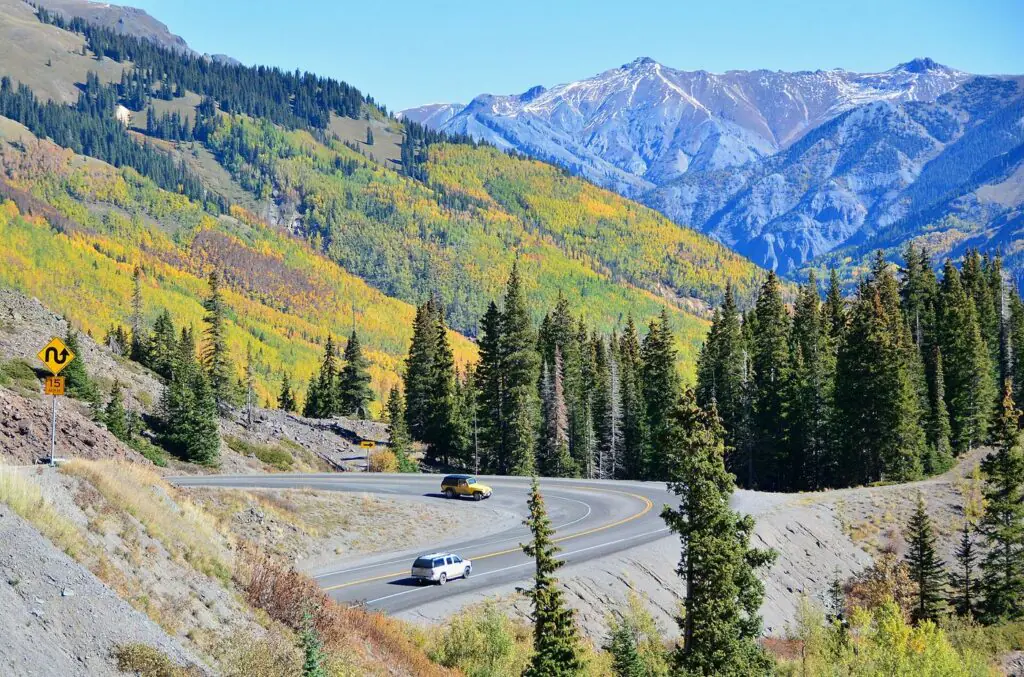 A car on the winding Million Dollar Highway between Silverton and Ouray, Colorado, framed by autumn aspens and snow-capped peaks